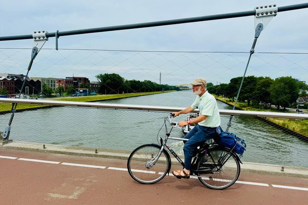 A cyclist riding across a red asphalt cycle track on a cable-stayed bridge over a canal.
