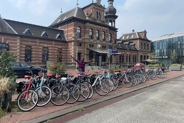 A row of rental bicycles lined up in front of a historic railway station building.