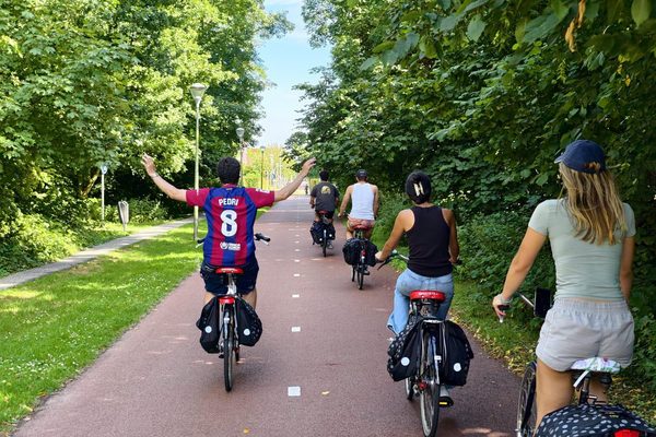 Participants cycling single file along a tree-lined red asphalt bike path, one rider with arms outstretched.