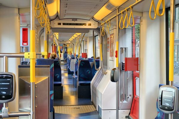 The interior of a nearly empty tram with yellow grab handles, blue seats, and ticket validators.
