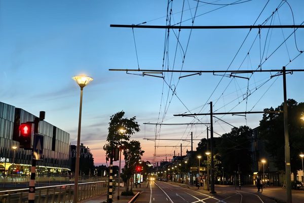 Tram tracks and overhead catenary wires converging along a city street at dusk.