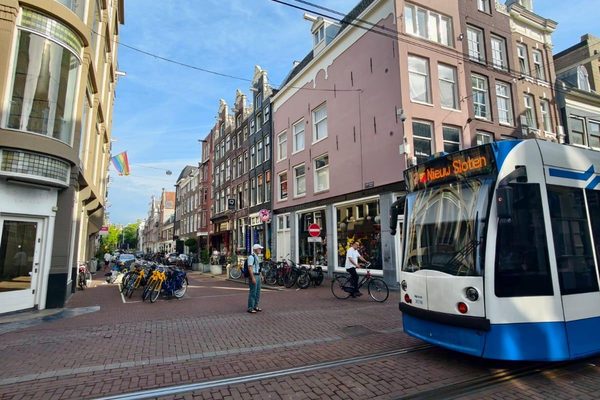 A city tram turning onto a brick street lined with historic gabled buildings and parked bicycles.