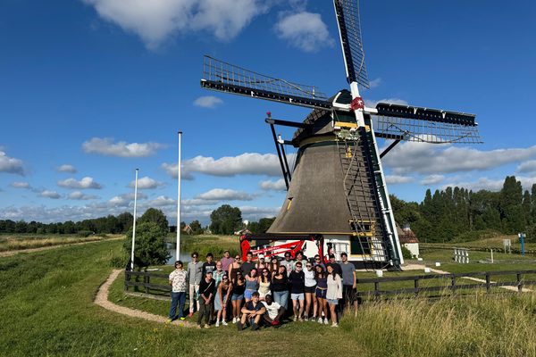 The program cohort posing together in front of a traditional Dutch windmill beside a canal.