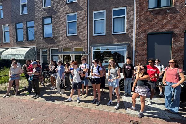 A group of participants on a brick-paved sidewalk in front of Dutch townhouses during a walking tour.